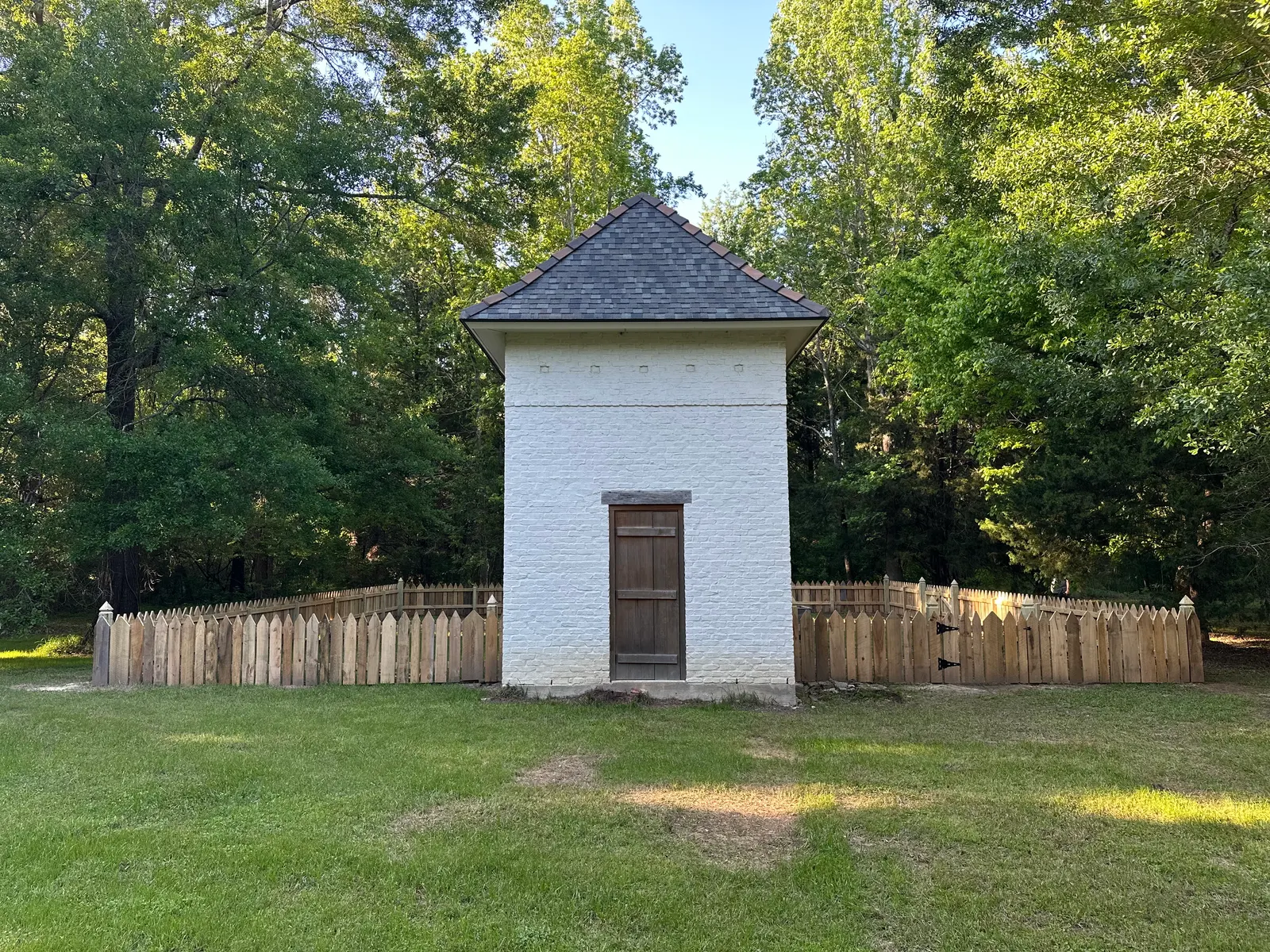 Front elevation of a white brick pigeonnier enclosed by a custom cypress picket fence