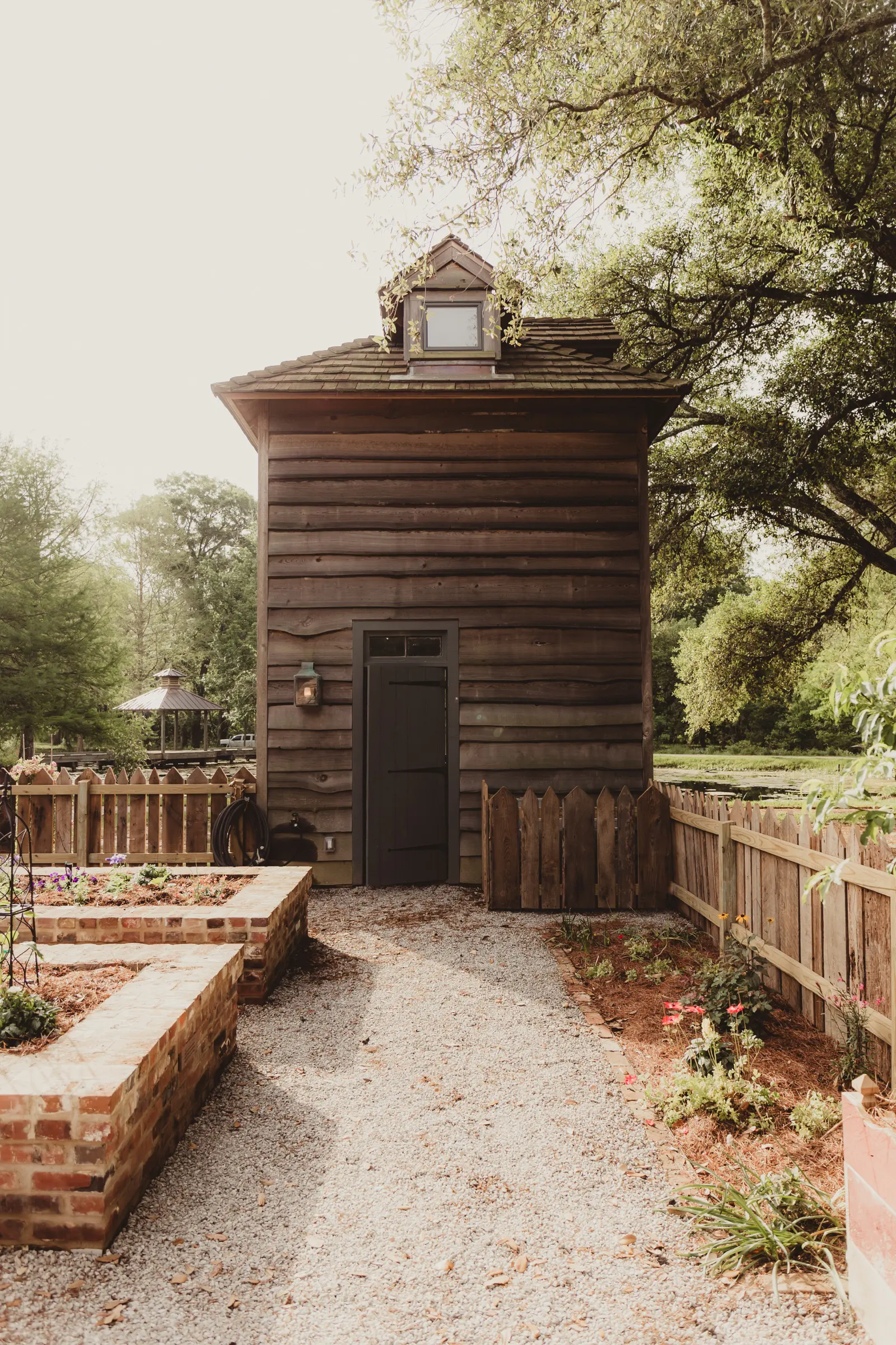 Custom wood picket fence lining a garden path beside a weathered farm building